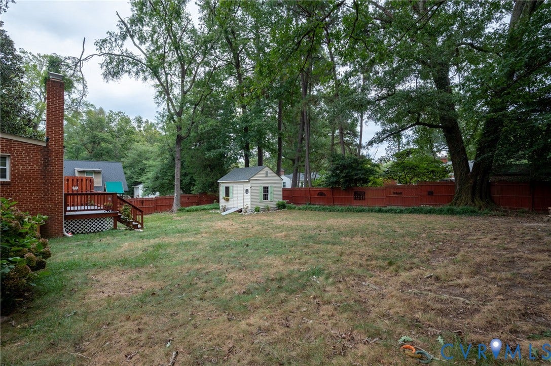 3353 Warner Road, Stratford Hills, Richmond, VA 23225 Expansive backyard featuring a red wood-panel fence, mature trees, a detached shed, and a wood deck with lattice skirting
