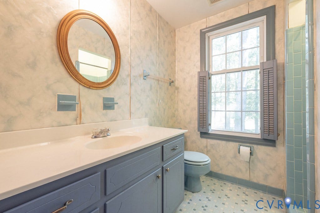 13830 Hailsham Circle, Salisbury, Midlothian, VA 23113 White countertop vanity with built-in sink and blue cabinetry, framed oval mirror, grid window with louvered shutters, and tiled flooring