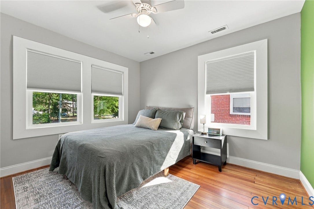 3504 Delaware Avenue, Richmond, VA 23222 Hardwood flooring, three windows with cellular shades, a ceiling fan with integrated lighting, and a nightstand with an open shelf