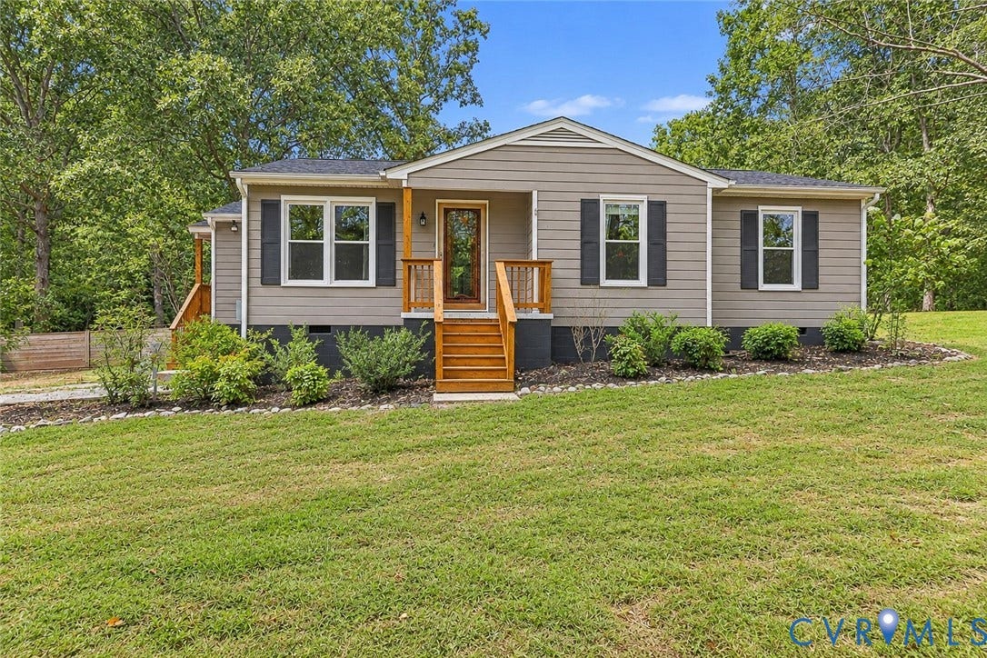 Siding exterior with dark shutters, front porch with wood railings and steps, established landscaping, and a sloped lawn