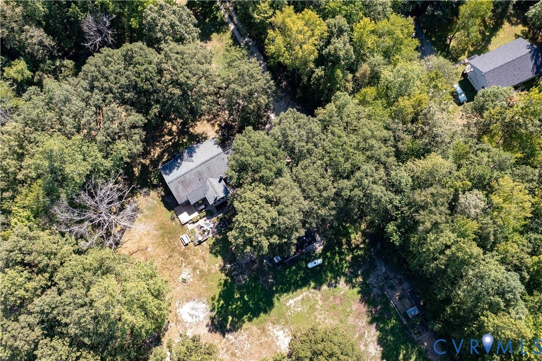 Wooded property with a single-story dwelling featuring a dark shingled roof and surrounded by mature trees