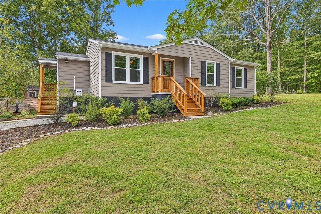 Siding exterior with dark shutters, natural wood-tone railings, gravel pathway, and mature landscaping