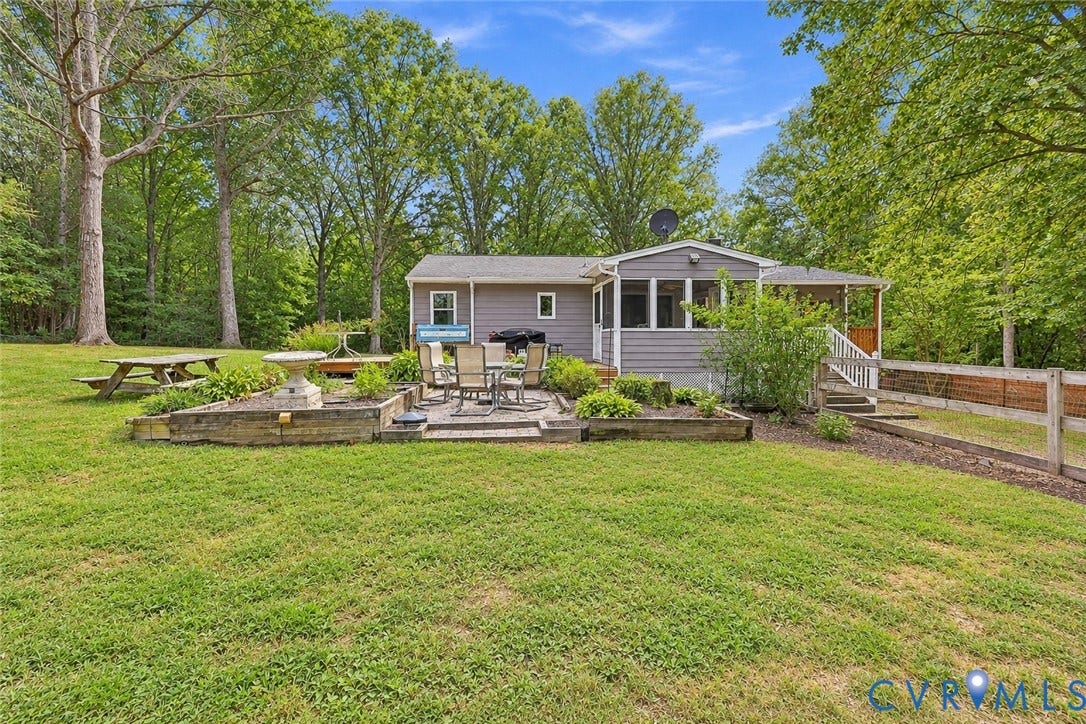 Expansive yard with mature trees, a stone patio, and a raised garden bed