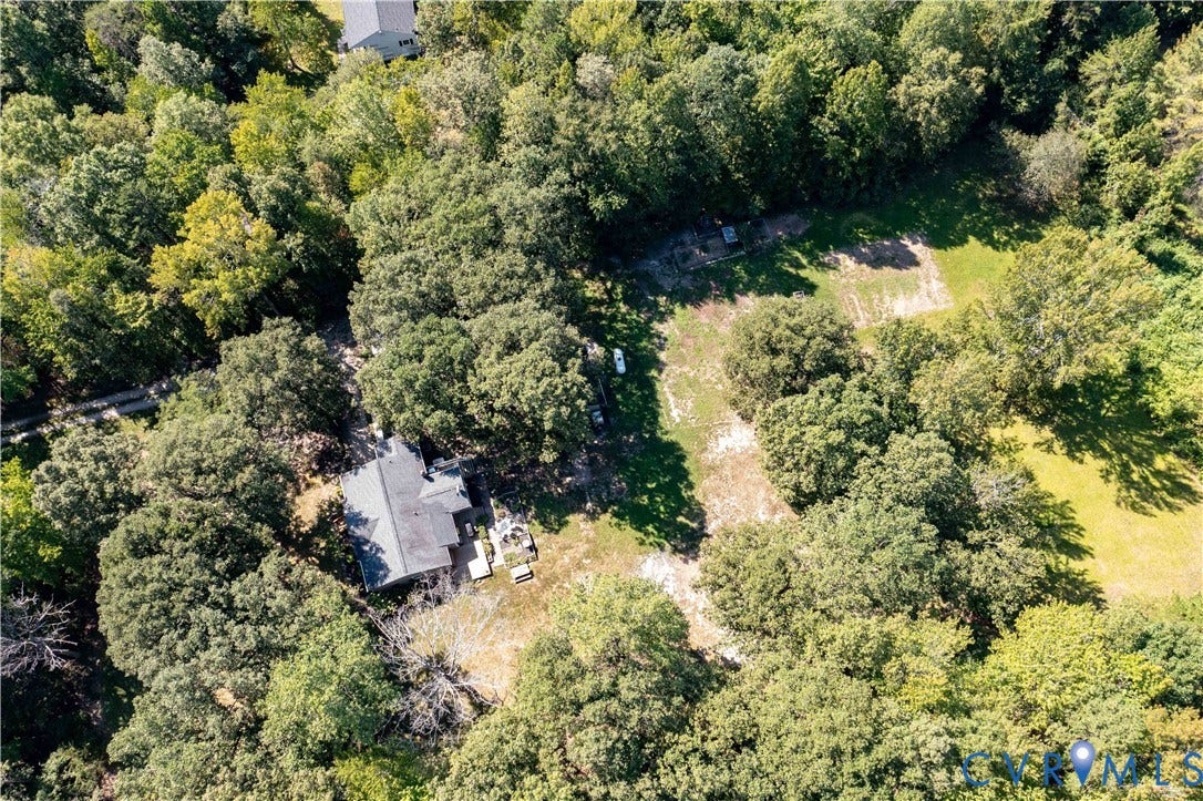 Property surrounded by mature trees, featuring a dark shingle roof and a cleared, grassy area