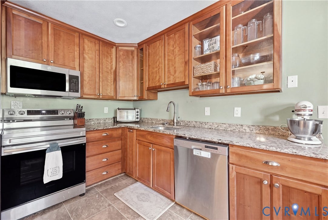 Warm wood cabinetry, granite-style countertops, integrated stainless steel appliances, and glass-front upper cabinets define this kitchen space