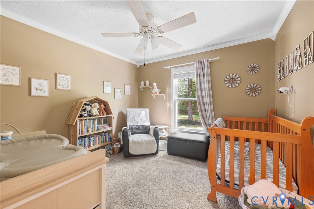 Neutral tone painted walls, white crown molding, light-colored ceiling fan, carpet flooring, and a window with exterior visibility