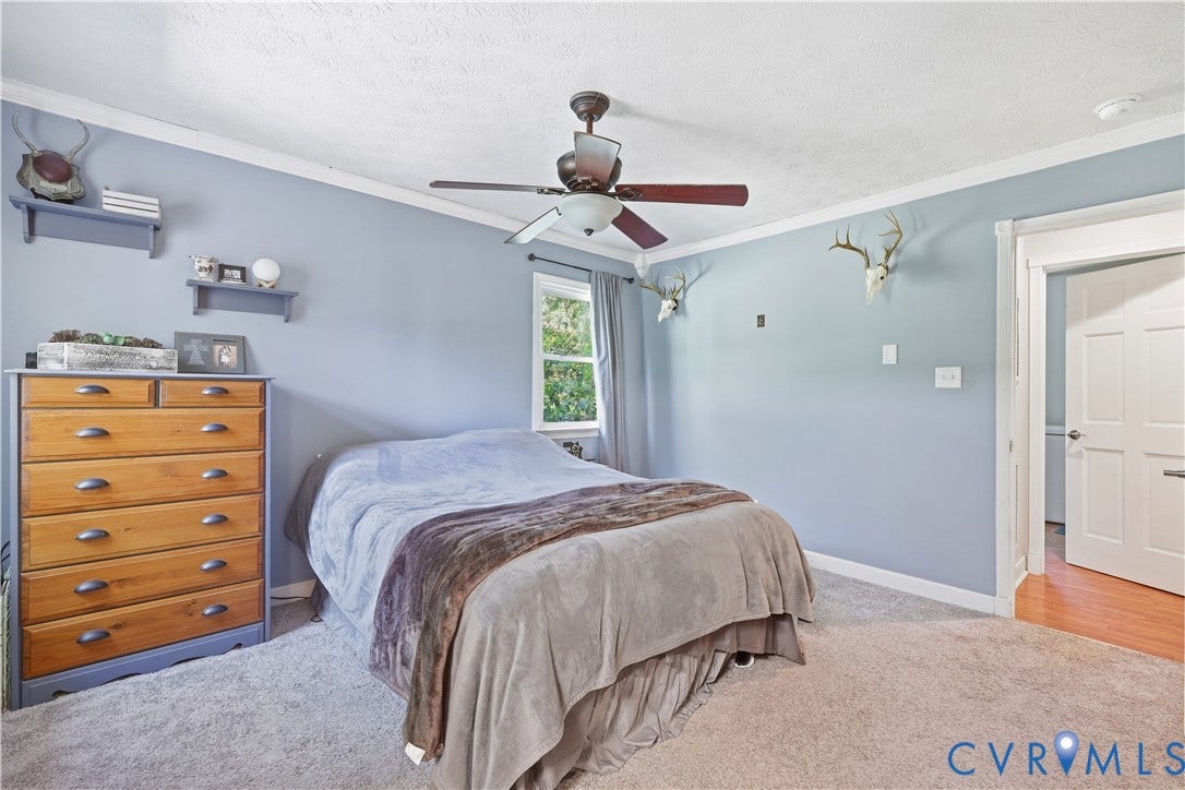 Carpeted flooring, crown molding, ceiling fan with integrated lighting, window with exterior view, and a wood-finish interior door