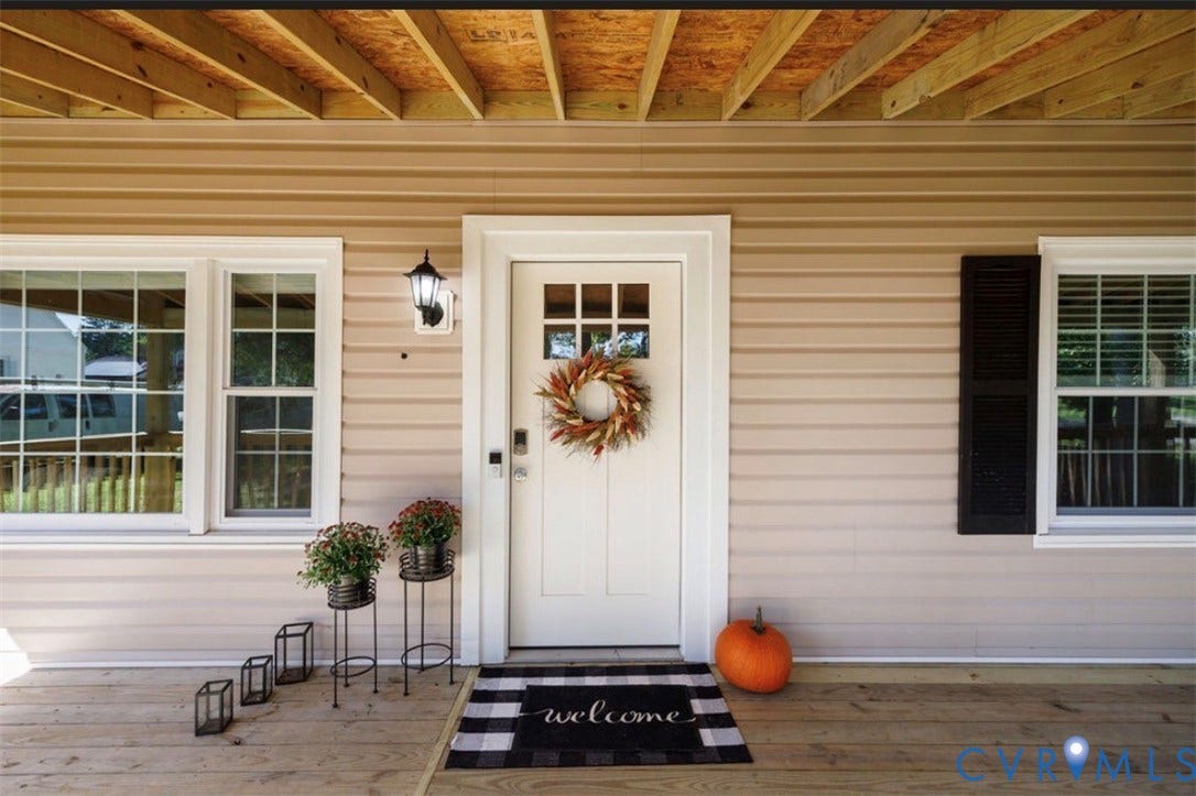 Porch entry with wood flooring, beige siding, white-framed windows, a white front door with lites, and an exterior wall lantern