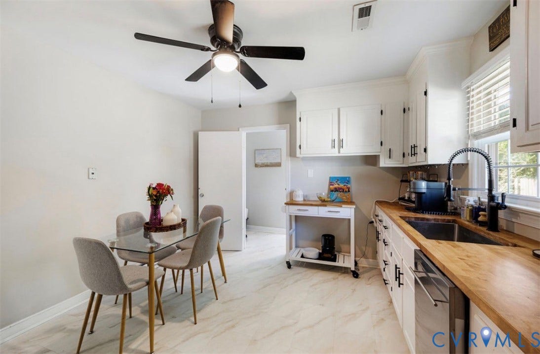 White shaker-style cabinetry with matte black hardware, wood-finish countertops, stainless steel undermount sink with a black pull-down faucet, and light-toned tile flooring