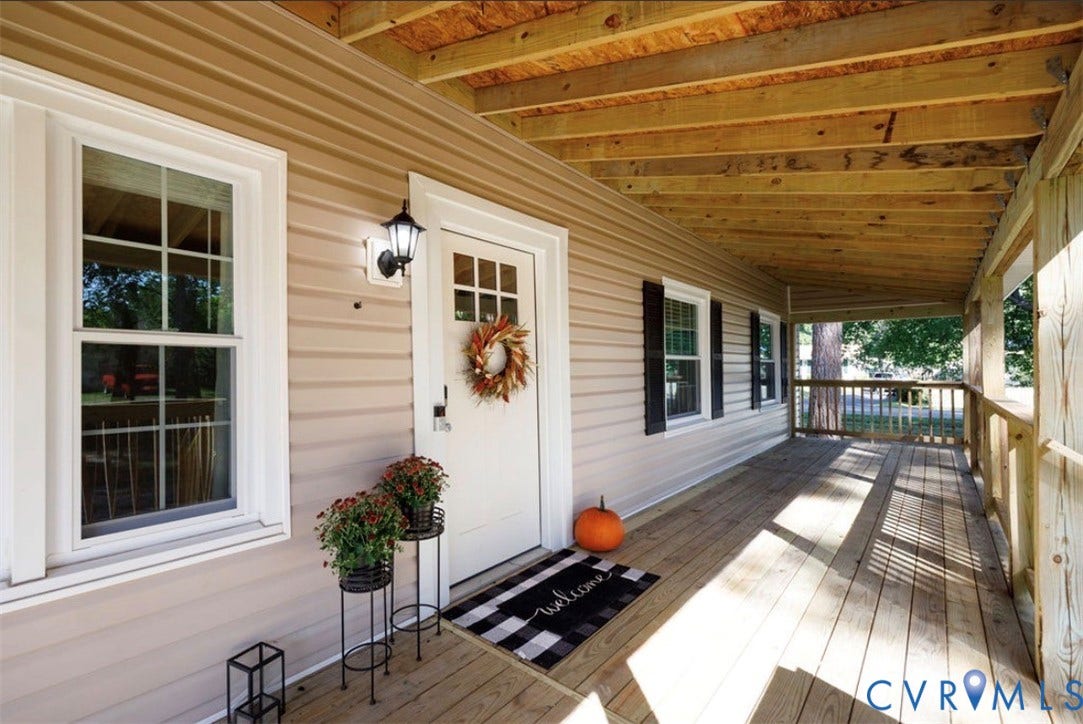 Spacious covered porch with natural wood flooring and exposed wood ceiling beams