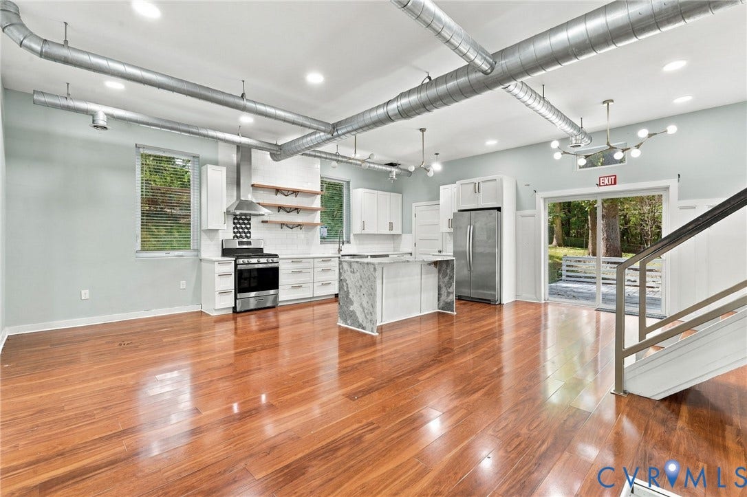 5824 Riverside Drive, Richmond, VA 23225 Expansive room featuring rich wood-finish flooring, a kitchen with white cabinetry and stainless steel appliances, a center island with a stone-finish countertop, exposed ductwork, and a sliding glass door