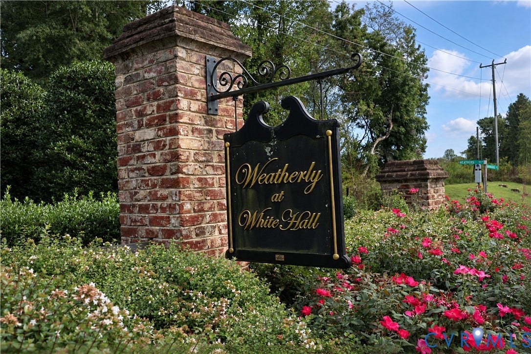 Brick pillar entryway featuring an ornamental sign, surrounded by blooming shrubs and manicured landscaping