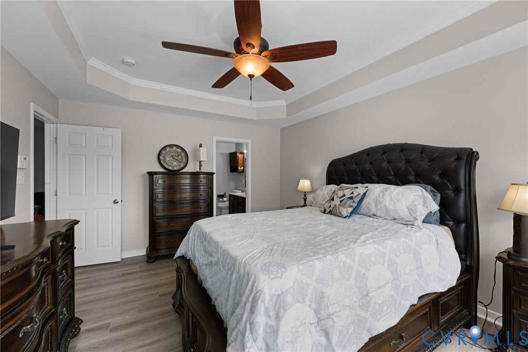 Tray ceiling with crown molding, ceiling fan, wood-finish flooring, and white paneled doors
