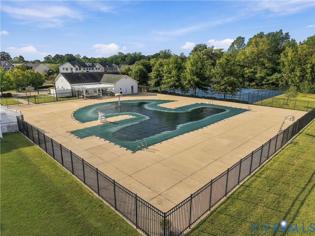 Community pool area featuring a large covered pool, concrete pool deck, black metal fencing, and tennis courts