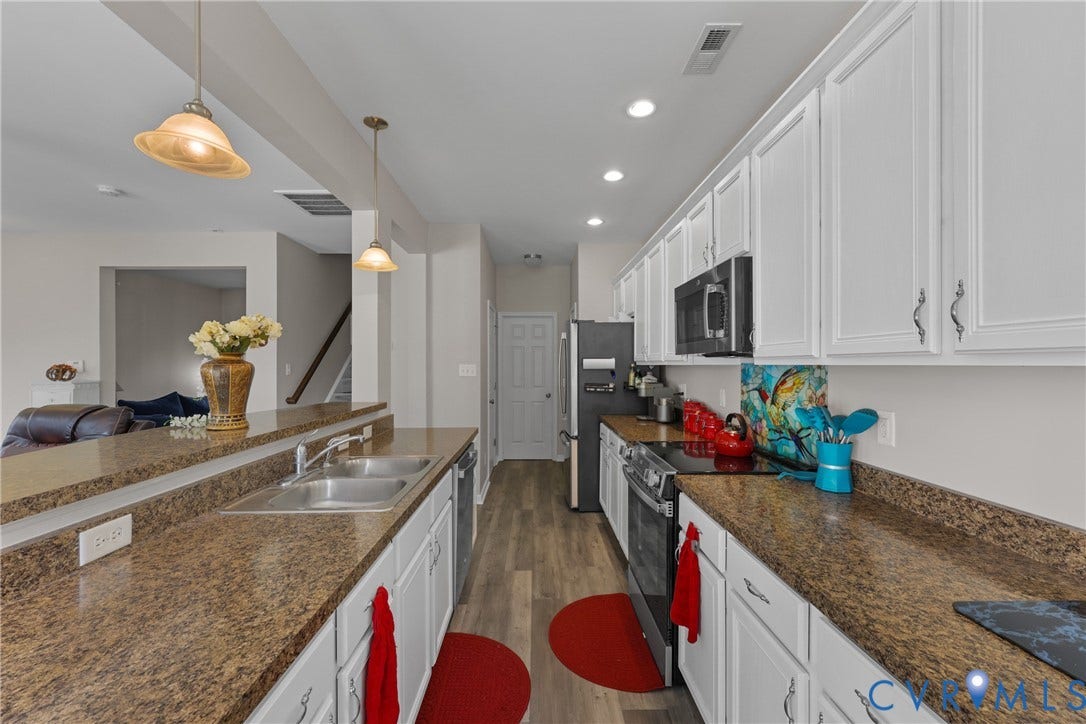 Kitchen featuring wood-finish flooring, white cabinetry, a double basin sink, and pendant lighting