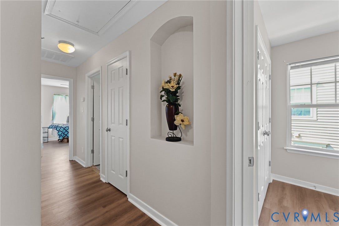 Wood-finish flooring throughout, arched wall niche, multiple panel doors, and a window with blinds