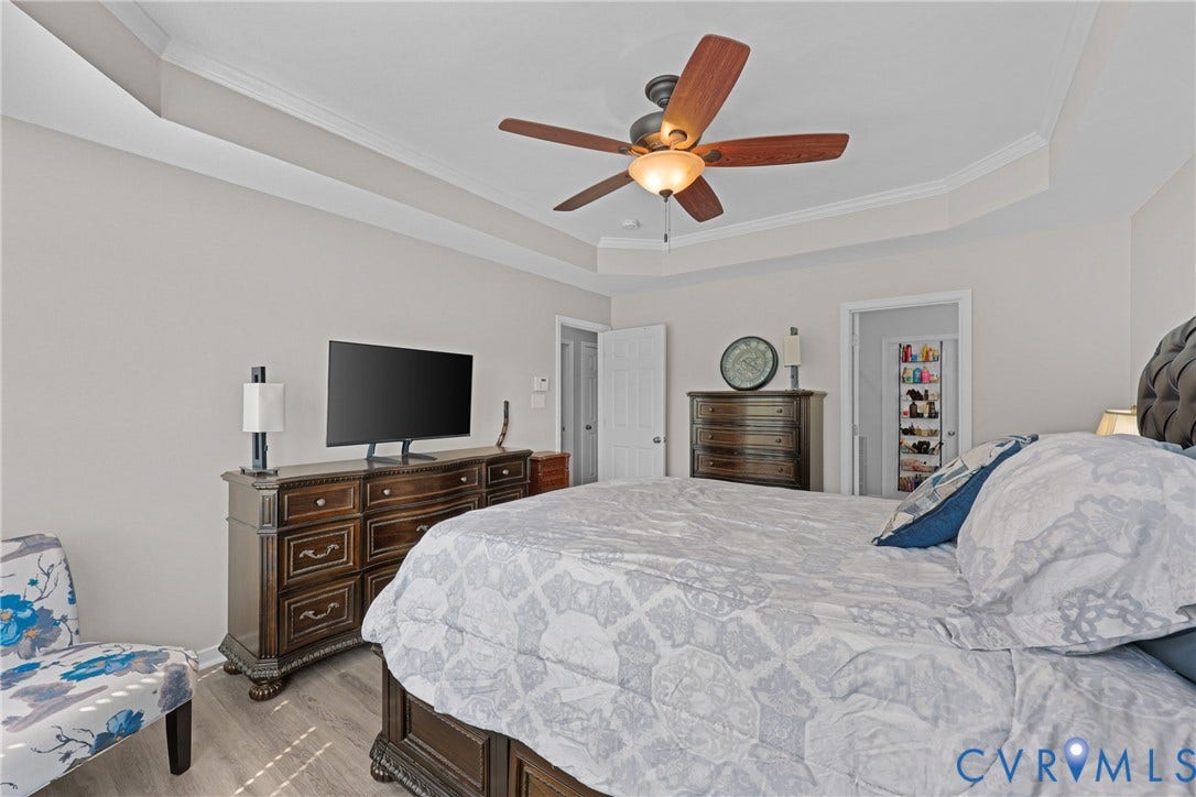 Tray ceiling with crown molding, ceiling fan with light fixture, wood-finish flooring, and painted interior walls