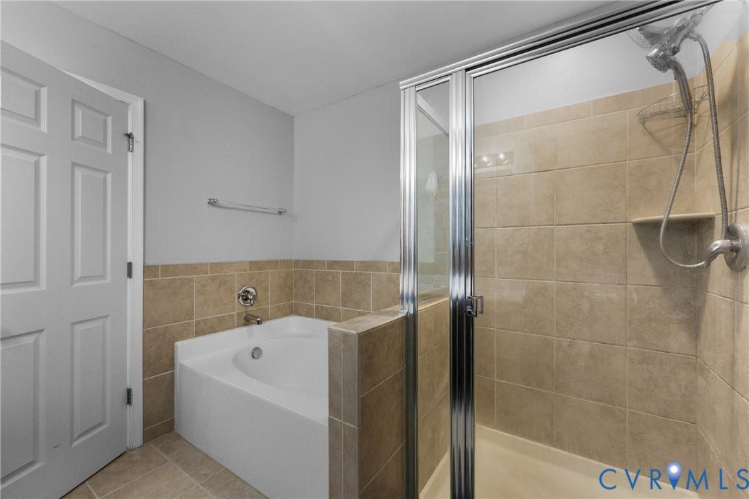Corner soaking tub, separate shower with glass enclosure, tiled walls and flooring, and brushed nickel fixtures