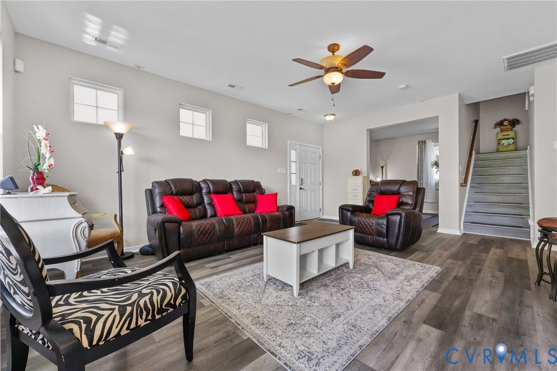 Wood-finish flooring throughout, ceiling fan with integrated lighting, multiple windows providing natural light, and a visible staircase with wood railing