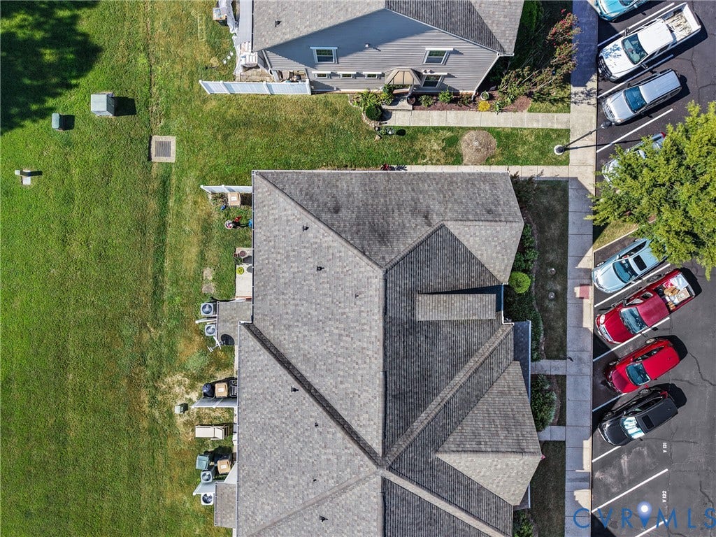 Paved parking area, mature tree canopy, residential buildings with gabled roofs, manicured lawn