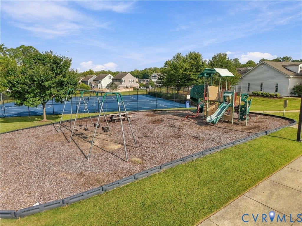 Playground area featuring swings, slides, a tennis court, and manicured green spaces
