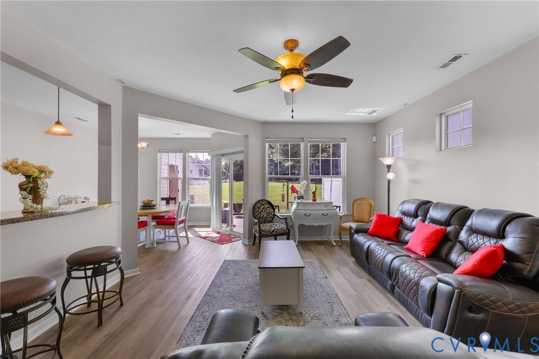Wood-finish flooring throughout, ceiling fan with integrated lighting, multiple windows providing natural illumination, and a breakfast bar with a granite-style countertop