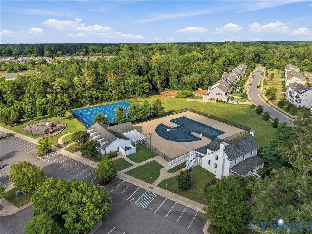 Outdoor community pool with surrounding paved deck, adjacent clubhouse building, and basketball court