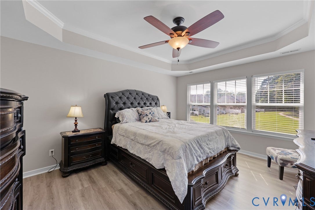 Tray ceiling with crown molding, wood-finish flooring, and a ceiling fan with integrated lighting