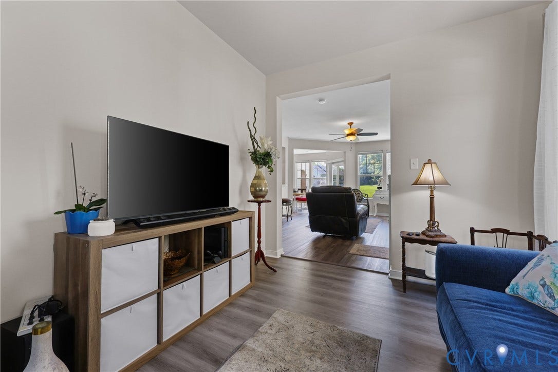 Wood-finish flooring throughout, light neutral wall paint, and a wide cased opening to an additional room