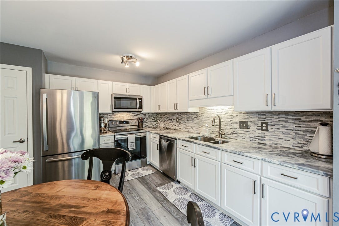 White cabinetry with silver-tone hardware, stainless steel appliances, mosaic tile backsplash, and light-tone countertops
