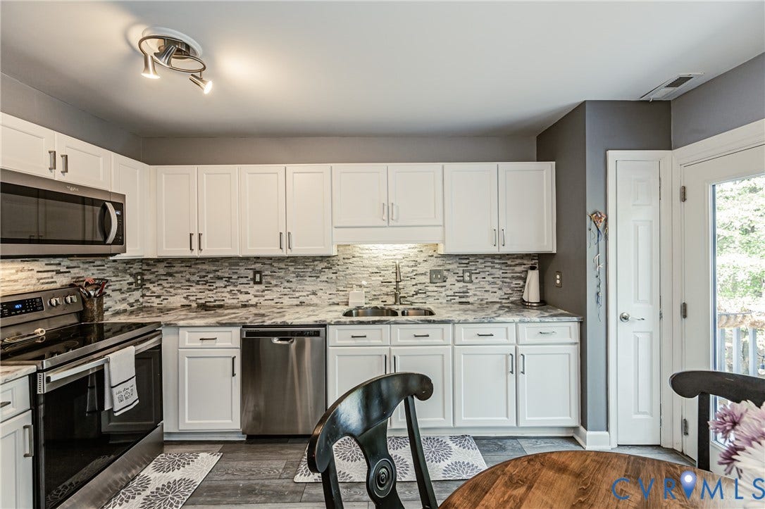 Kitchen featuring white cabinetry, stainless steel appliances, mosaic tile backsplash, and light-toned countertops