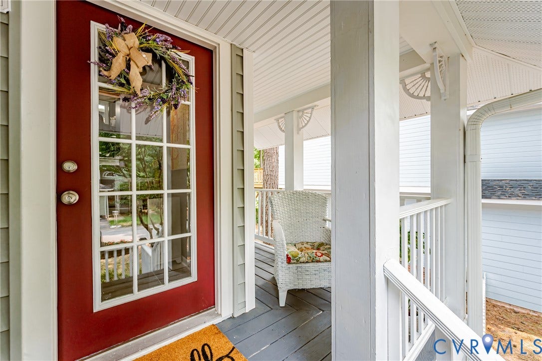 Front porch featuring a red entry door with glass panels, beadboard ceiling, white balustrade, and decorative porch brackets