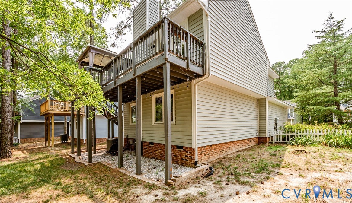 Multi-level exterior decking with wooden railings, light-colored siding, and a partial brick foundation