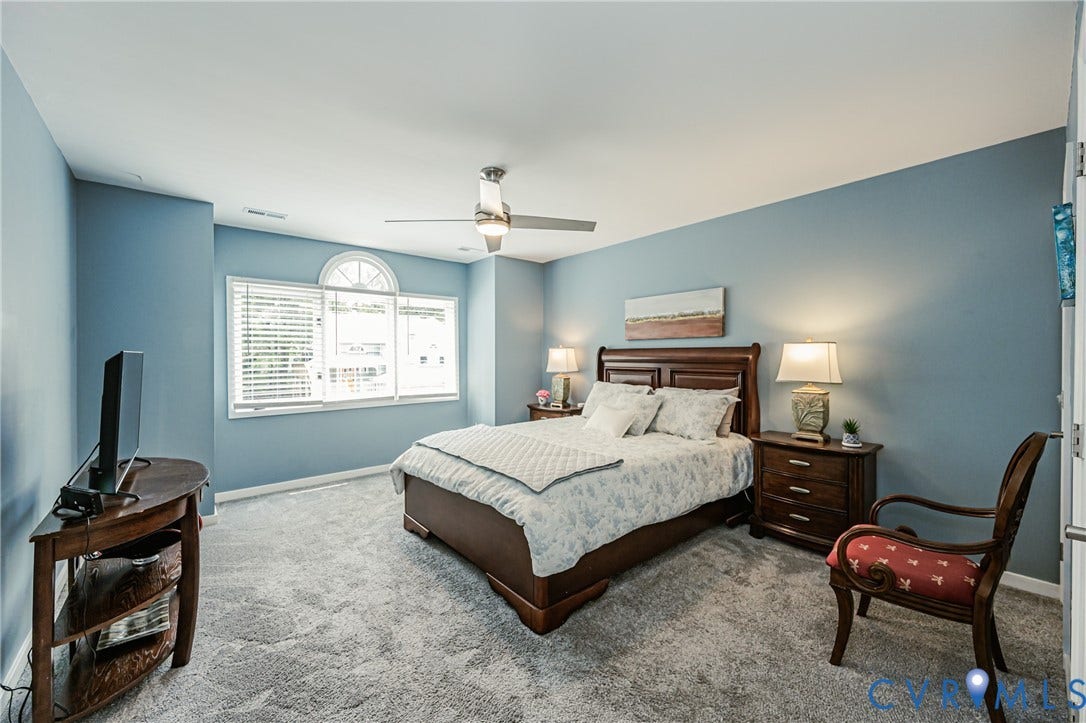 Carpeted room featuring a ceiling fan, arched transom window, and horizontal blinds