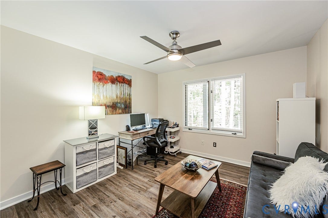 Wood-finish flooring throughout, featuring a double window, ceiling fan with integrated lighting, and neutral wall paint