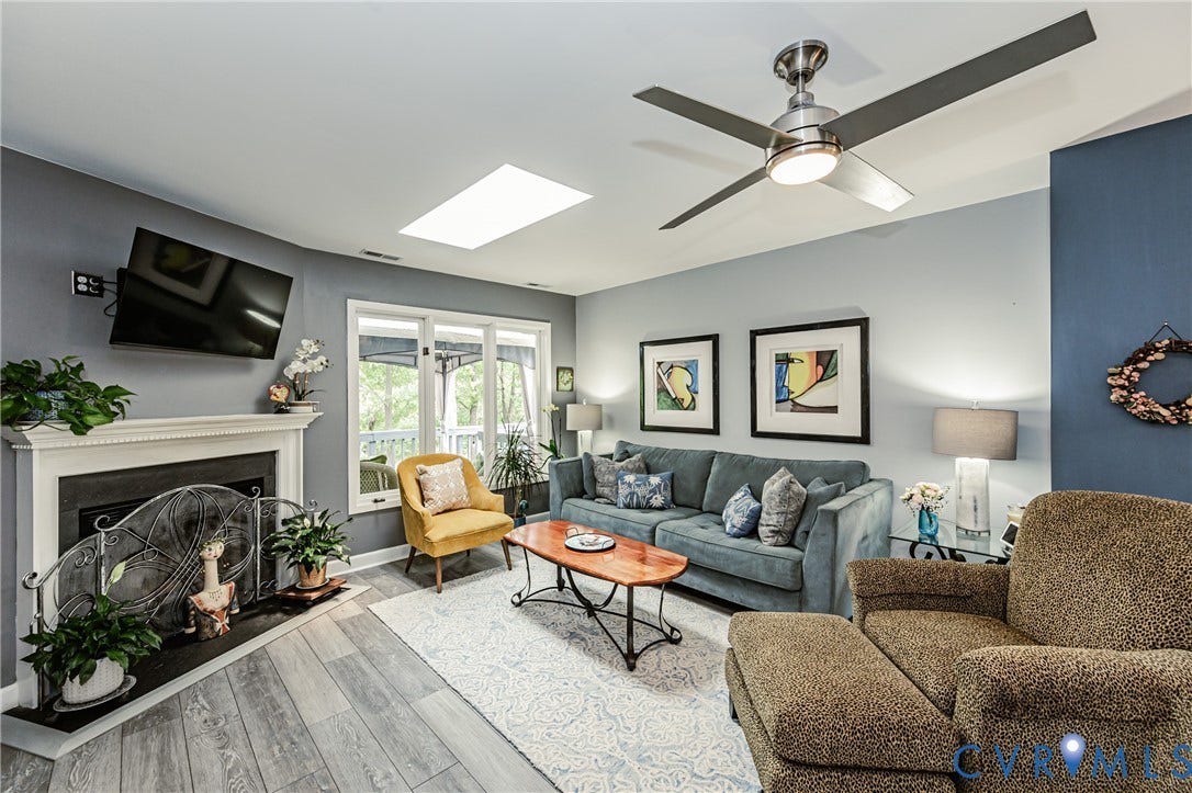 Living area featuring a fireplace with a white mantel, wood-finish flooring, and a ceiling fan