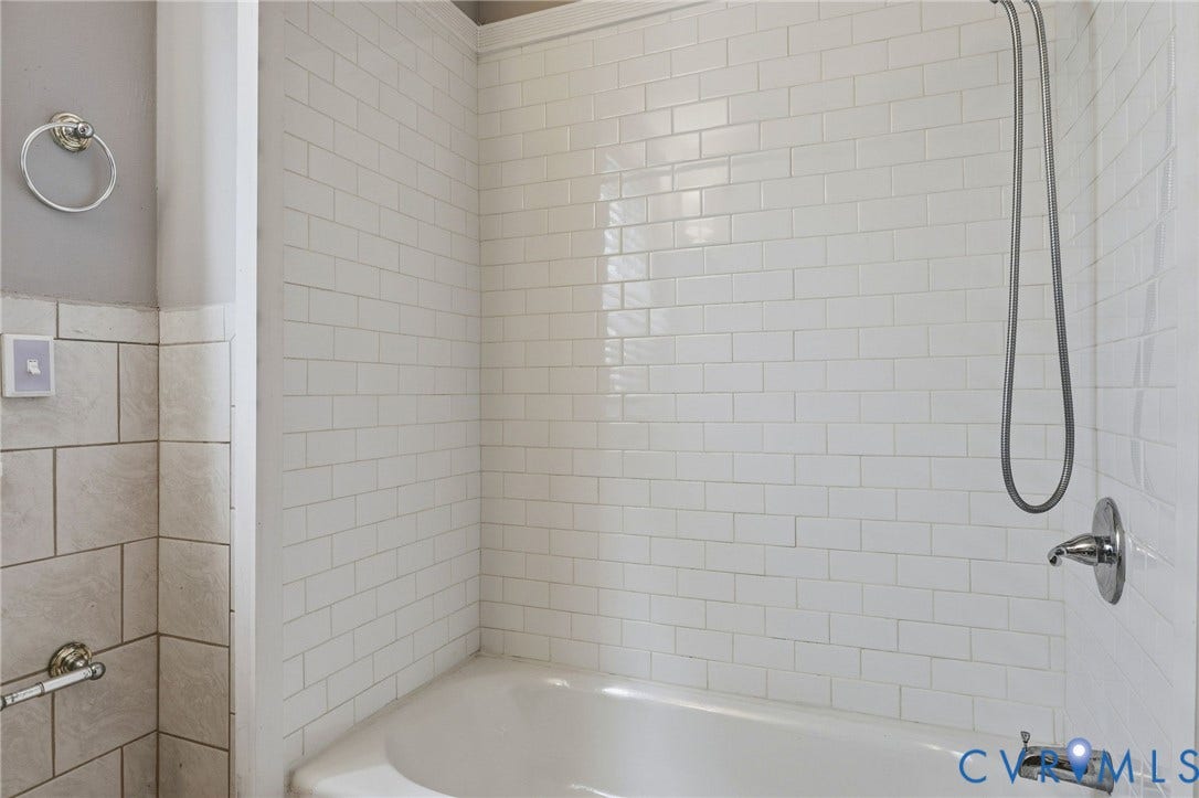 Bathtub with white subway tile surround, chrome shower fixture, and handheld shower sprayer