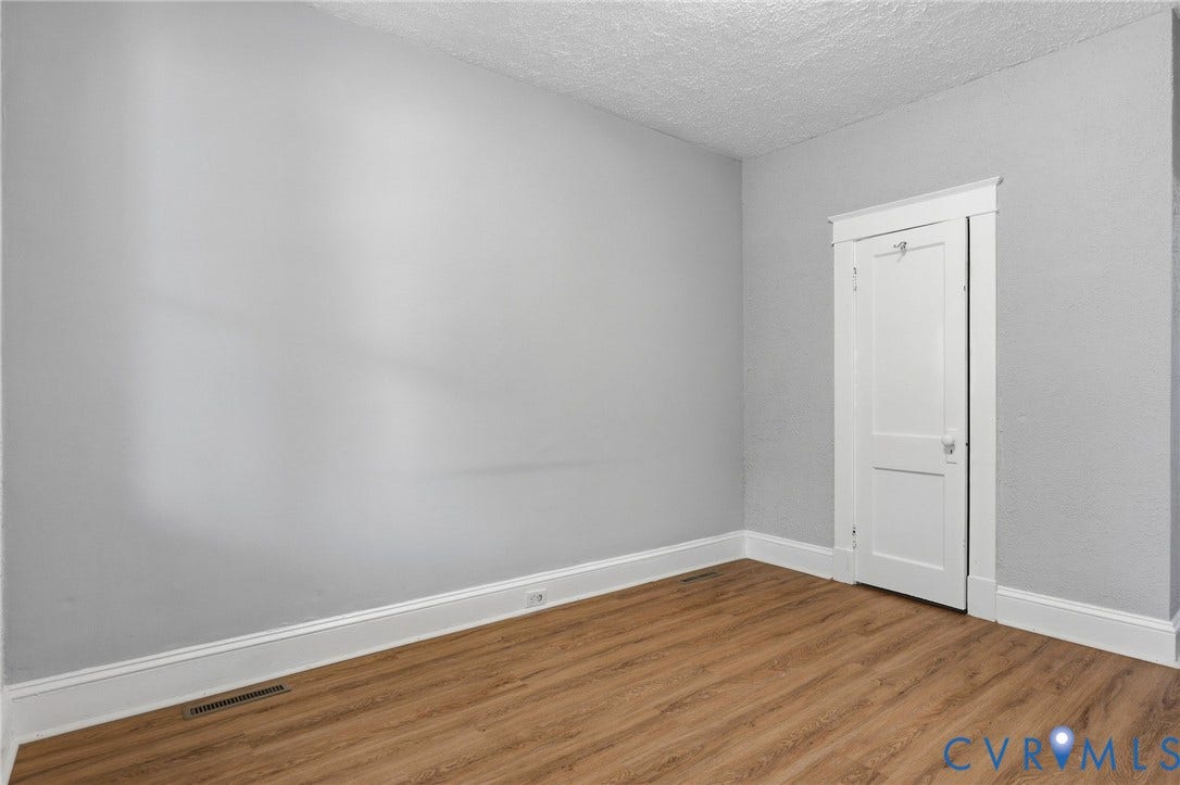 Gray painted walls, wood-finish flooring, white trim, and a white interior door