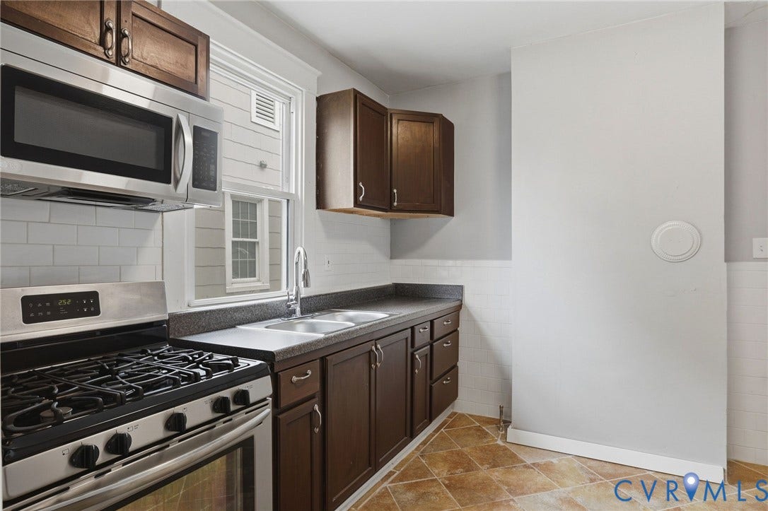 Stainless steel range, coordinating microwave, subway tile backsplash, dark wood-finish cabinetry, and a dual basin sink