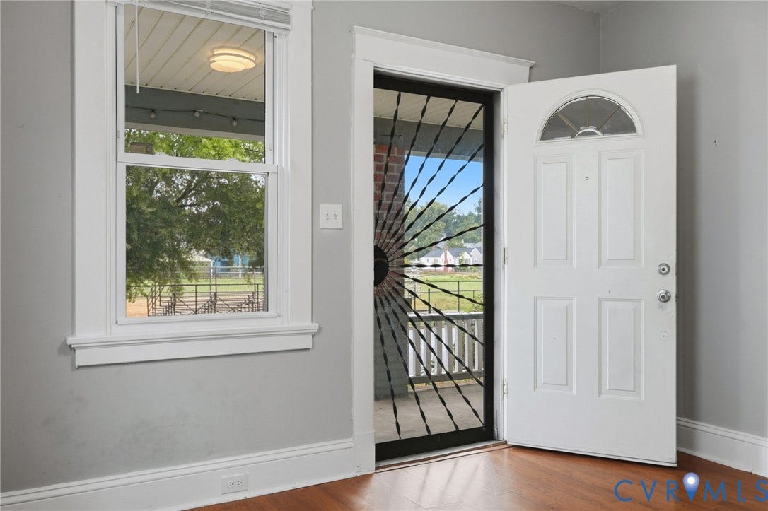 Hardwood-finish flooring, white trim, and a white door with an arched window accent