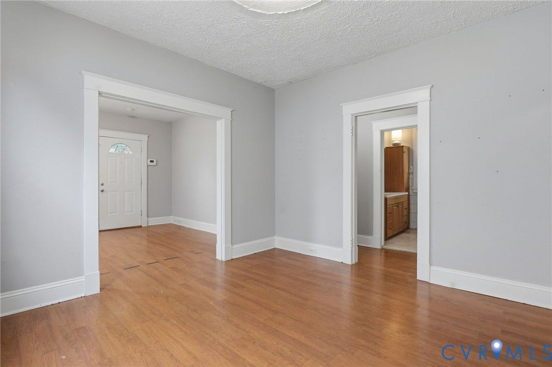 Hardwood-finish flooring throughout, light gray wall paint, white trim, and a white entry door with an arched glass insert