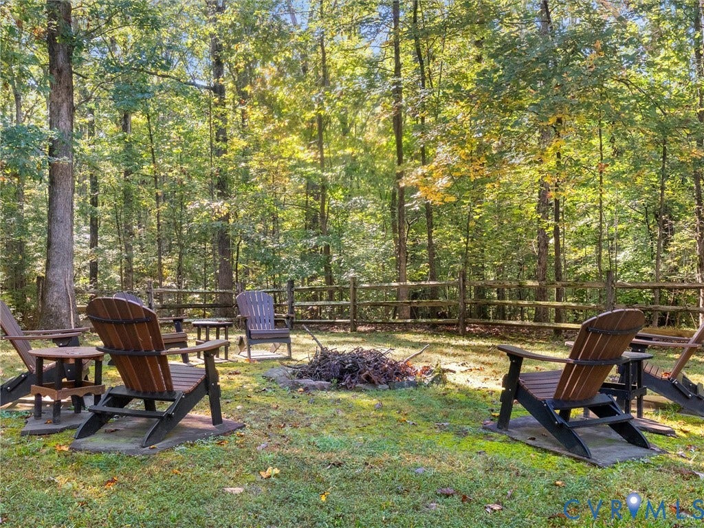 3801 Old River Trail, Powhatan, VA 23139 Backyard area featuring a stone-lined fire pit, split-rail wood fencing, and mature woodland surroundings