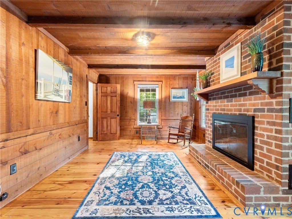 3801 Old River Trail, Powhatan, VA 23139 Interior featuring knotty wood wall paneling, exposed wood ceiling beams, wood-finish flooring, and a brick fireplace with a wood mantel