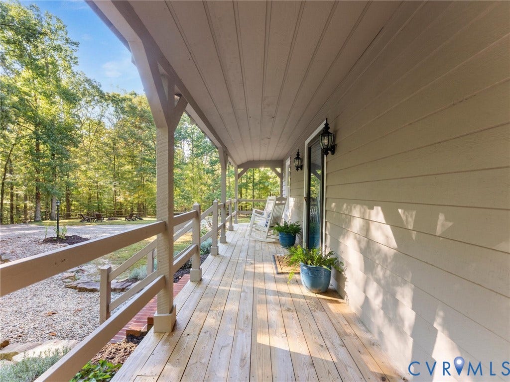 3801 Old River Trail, Powhatan, VA 23139 Covered wood-plank porch featuring horizontal siding, decorative wood brackets, post-and-rail timber fencing, and wall-mounted exterior lanterns