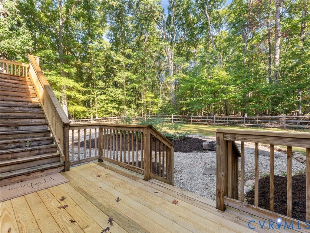 3801 Old River Trail, Powhatan, VA 23139 Elevated wood deck featuring vertical wood balusters and a staircase, overlooking a fenced backyard with mulched landscaping and stone ground cover