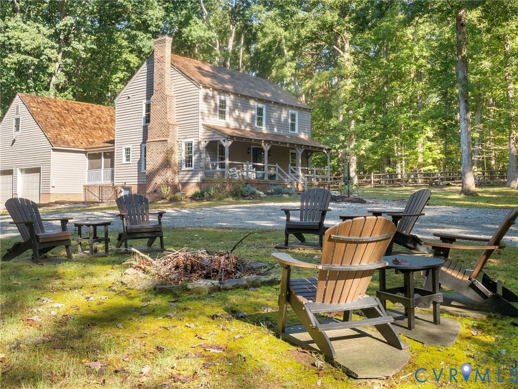 3801 Old River Trail, Powhatan, VA 23139 Two-story exterior featuring a stone-clad chimney, covered front porch, attached garage, and stone fire pit set within a wooded lot