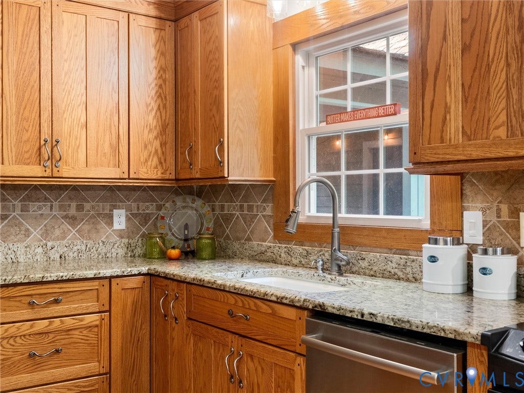 3801 Old River Trail, Powhatan, VA 23139 Custom natural wood cabinetry featuring brushed metal hardware, stone-patterned countertops, a stainless steel pull-down faucet, an undermount sink, and a decorative tile backsplash