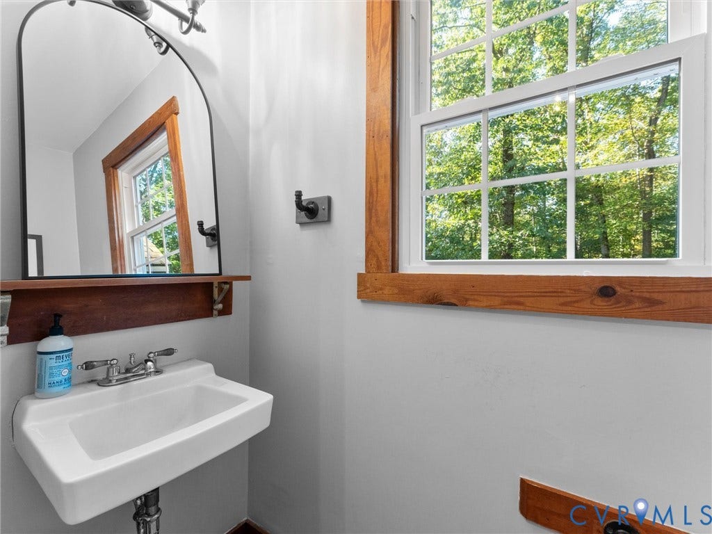 3801 Old River Trail, Powhatan, VA 23139 Wall-mounted porcelain sink with chrome fixtures, arched mirror, built-in wooden shelf, and natural wood window casing