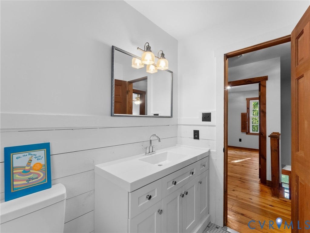 3801 Old River Trail, Powhatan, VA 23139 White shiplap walls paired with a white vanity featuring a rectangular integrated sink, chrome faucet, framed vanity mirror, and three-bulb vanity light