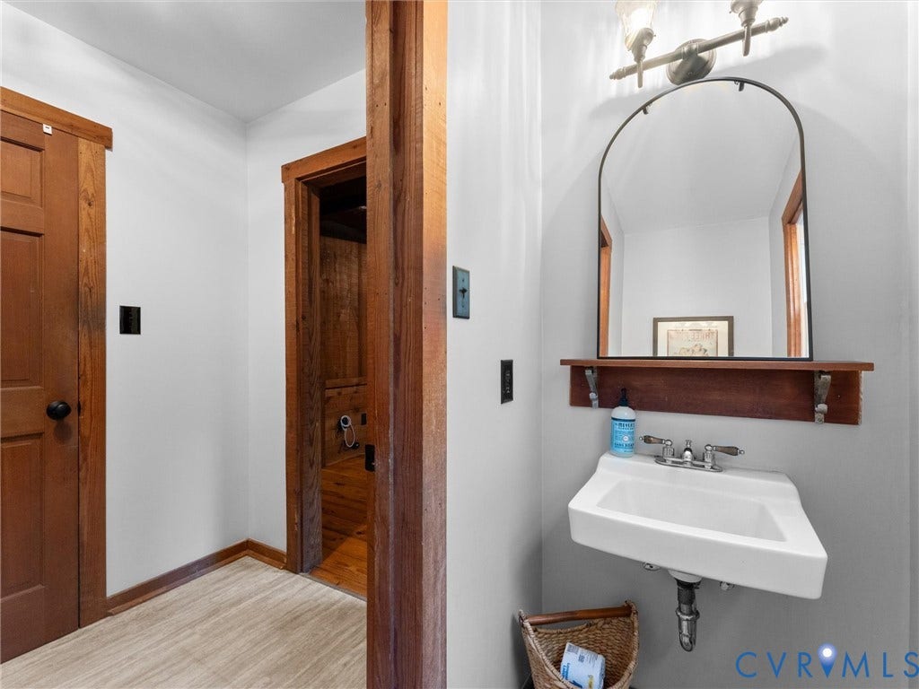 3801 Old River Trail, Powhatan, VA 23139 Wall-mounted porcelain sink with chrome fixtures, arched vanity mirror, wood-finish wall shelving, and natural wood door casings
